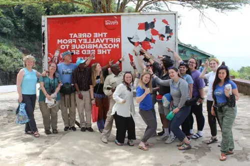 A group of students and others stand in front of a large sign with an illustrated map of Africa