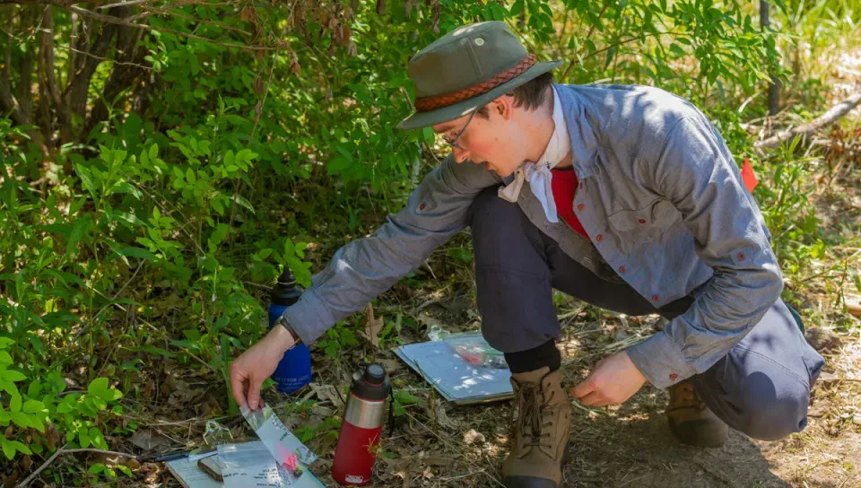 A U N E student picks up a plastic bag containing an artifact found at a dig site